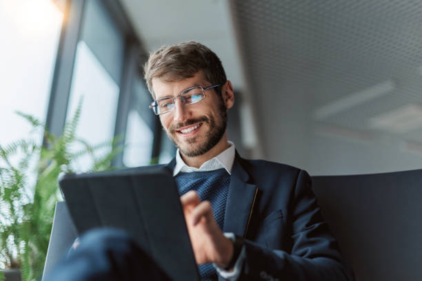 Smiling businessman in a suit uses a tablet, symbolizing success in Dubai Free Zones for business ventures.