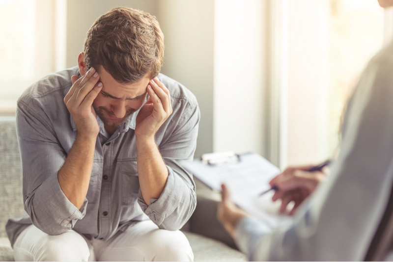 A troubled man holds his head in his hands while talking to a therapist.