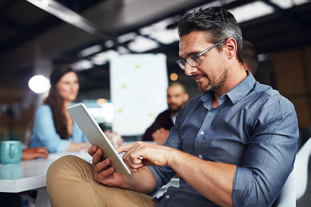 Business professional analyzing data on a tablet in a collaborative office environment.