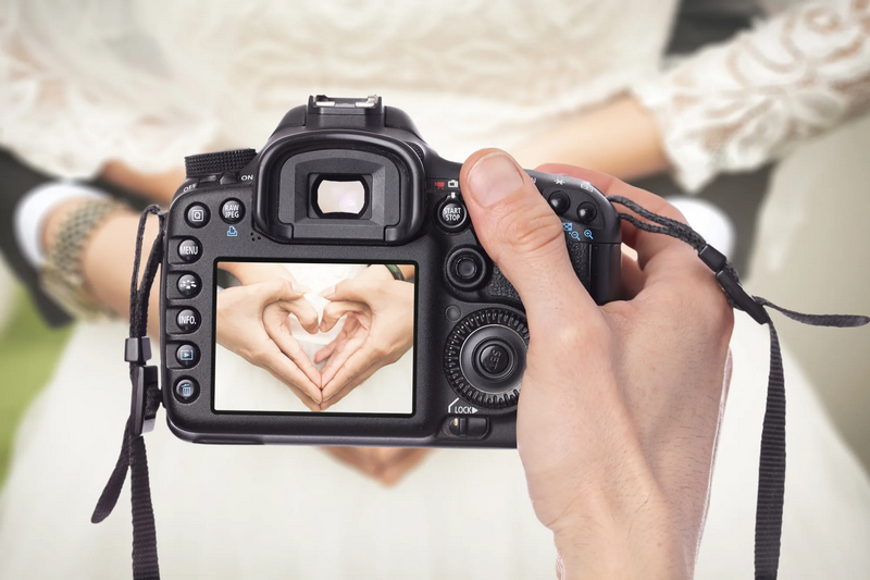 A person holds a camera displaying an image of hands forming a heart shape.